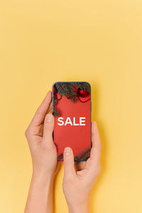 Cropped hand of woman holding mobile phone against yellow background