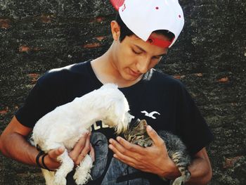 Teenage boy holding dog and kitten against wall