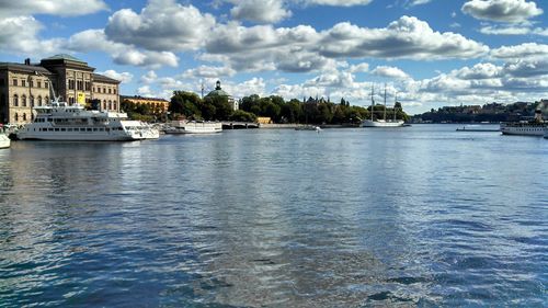 Boats in river against cloudy sky