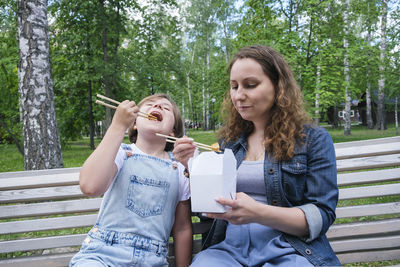 Mid adult mature woman and teenage girl on a summer day in the park has lunch with noodles wok
