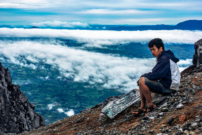 Side view of man looking away while sitting on mountain