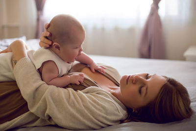 Young mother with red hair is lying on the bed with her daughter at home in the morning