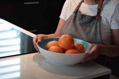 Midsection of woman holding oranges in bowl 