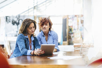 Professional mature businesswomen sharing tablet in light office