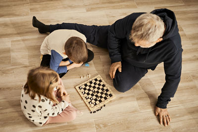 Sibling playing chess sitting with grandfather at home