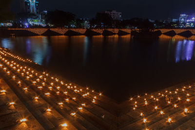 Illuminated buildings by river against sky at night