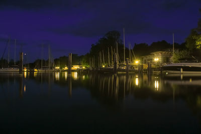 Illuminated city by river against sky at night