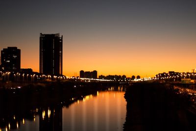 Illuminated city by river against sky at night