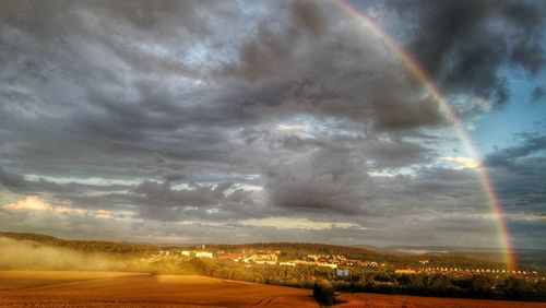 Scenic view of rainbow over landscape against cloudy sky