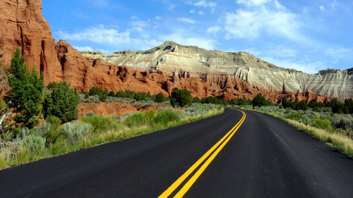 Empty road leading towards rocky mountains against sky