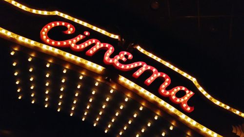 Low angle view of neon cinema sign at night
