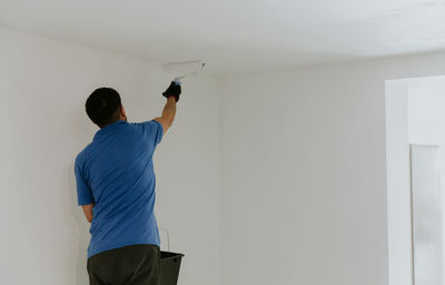 A young oriental man paints the ceiling with a roller.