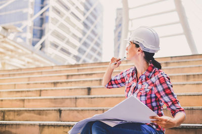 Architect holding blueprint while sitting in city