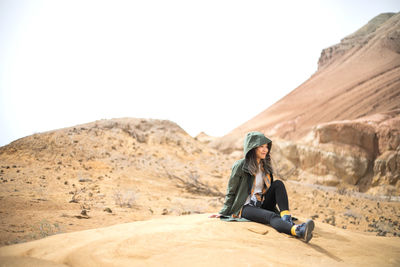 Woman sitting on rock against clear sky