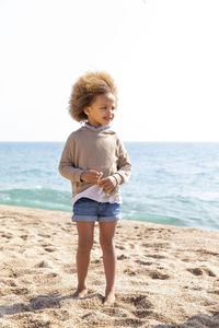 Cute girl with afro hairstyle standing in front of sea at beach