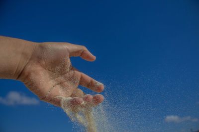 Cropped hand throwing sand against blue sky