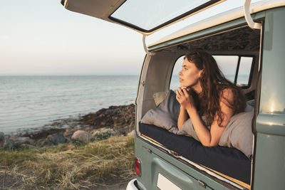 Young woman looking at sea while lying down in van