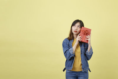 Portrait of young woman standing against yellow background