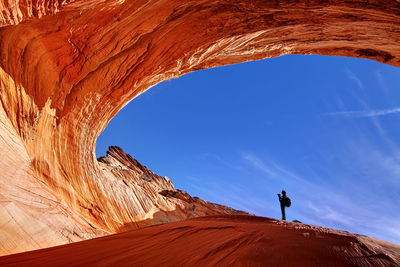 Low angle view of person standing at natural arch against blue sky