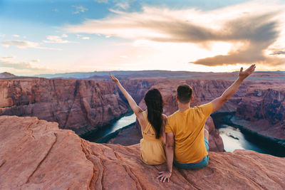 Rear view of man with arms raised standing on rock against sky