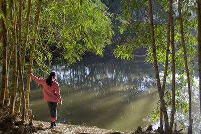 Rear view of man standing by lake in forest