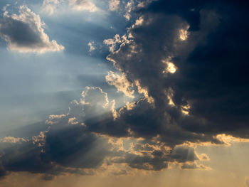 Low angle view of sunlight streaming through clouds