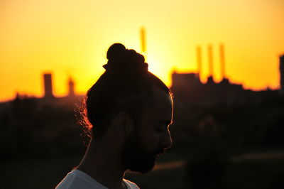 Close-up of man with hair bun against sky during sunset