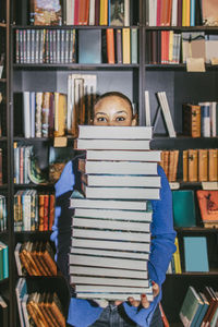 Portrait of young woman holding stack of books while standing in bookstore