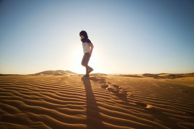 Man on sand dune in desert against clear sky