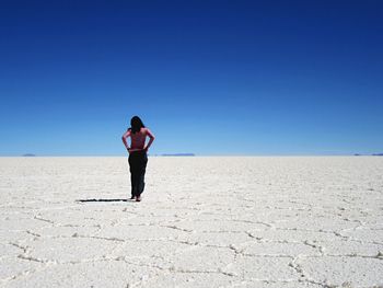 Rear view of mid adult woman standing on arid landscape against clear blue sky during sunny day