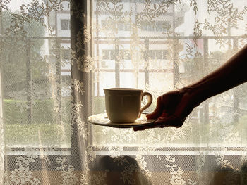 Hand holding coffee cup on window