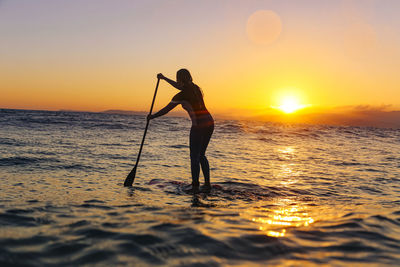 Female sup surfer at sunset time