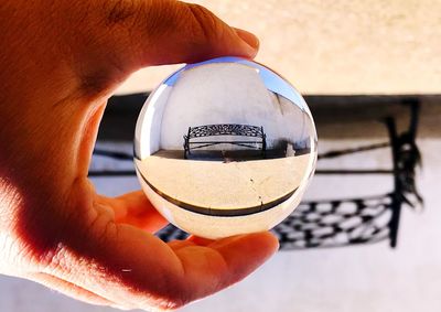 Cropped hand holding crystal ball with reflection of bench