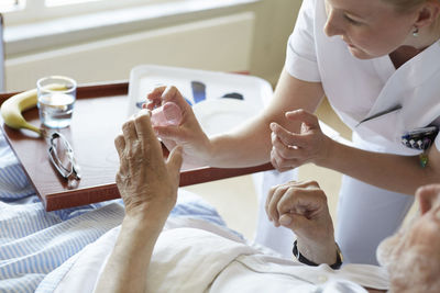 High angle view of female nurse giving cough syrup to senior man in hospital ward