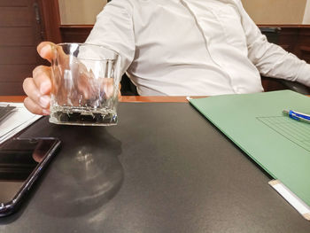 Midsection of man holding drink in glass on table