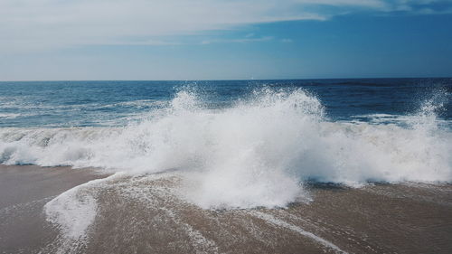 Scenic view of splashing waves against cloudy sky