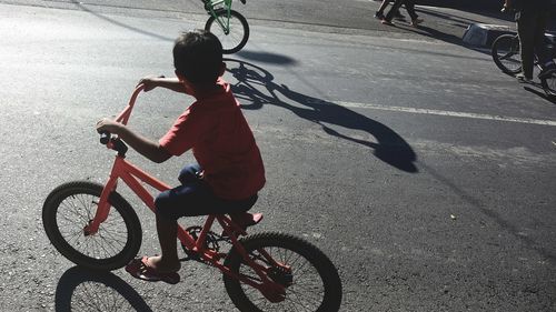 Boy riding bicycle on road during sunny day