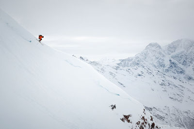 Side view of a man on skis in colorful clothes jumping from a mountain snowy slope against the