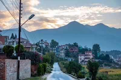 Road amidst buildings and mountains against sky at sunset