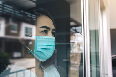 Close-up of woman wearing mask seen through window