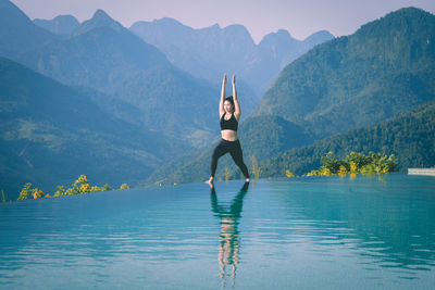 Full length of woman exercising at infinity pool against mountains