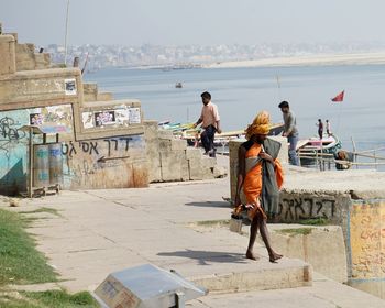 People walking on shore by city against sky