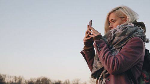 Woman holding mobile phone standing against sky