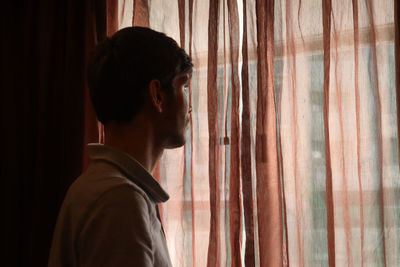 Young man standing against window at home