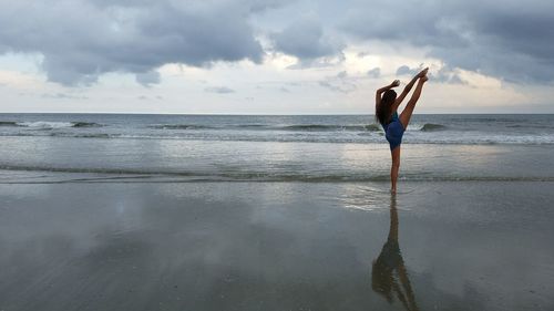 Rear view of woman exercising on shore at beach