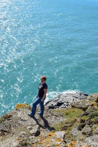 High angle view of smiling woman standing on cliff by sea