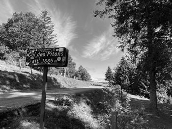 Road sign by trees against sky