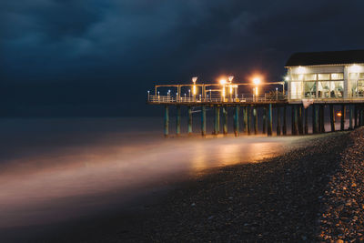 Illuminated pier over sea against sky at night