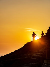 Silhouette people on mountain against orange sky