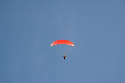 Red paraglider flying against clear blue sky, italy